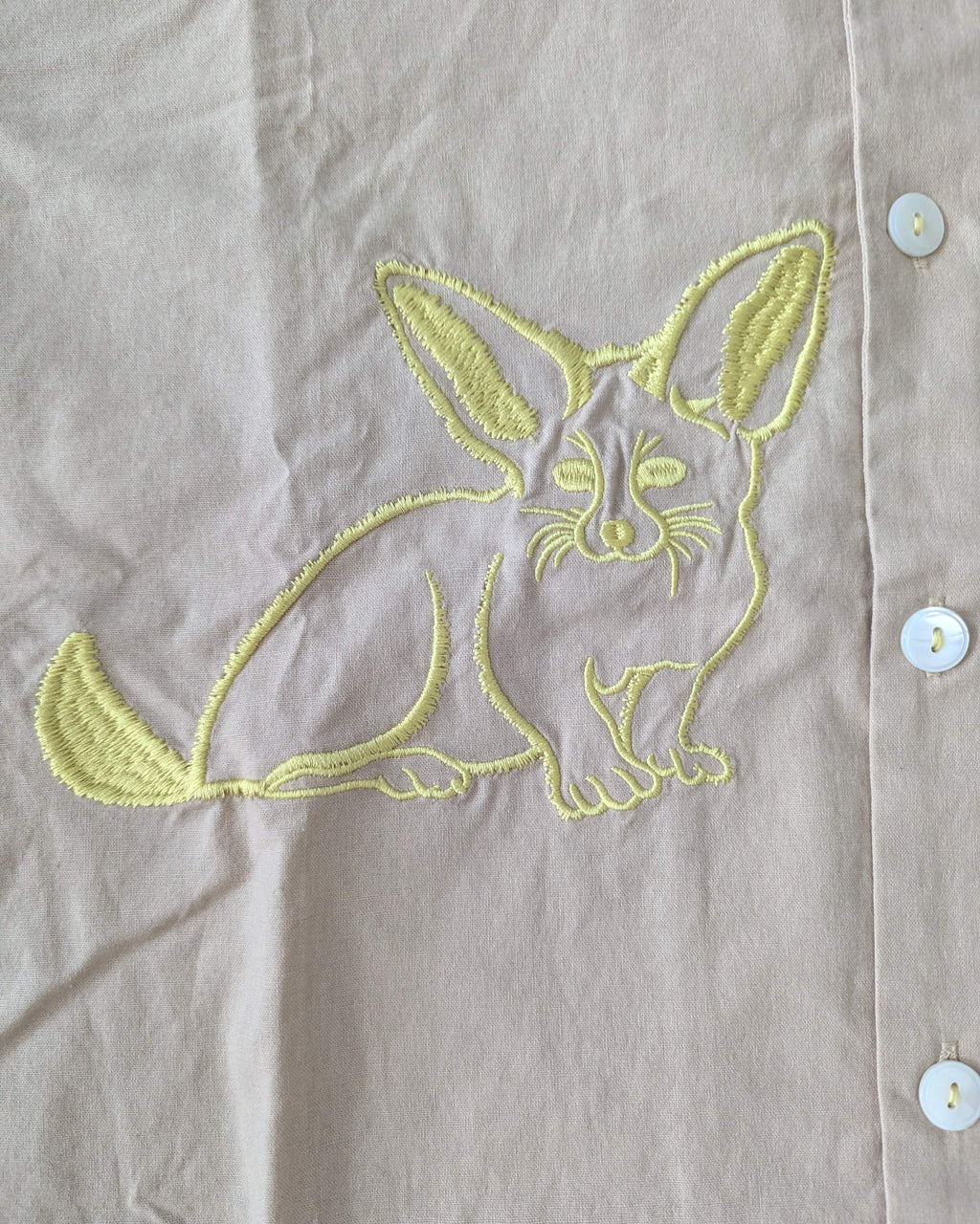 Embroidered canidae design on a light-coloured fabric with white buttons and yellow stitching.