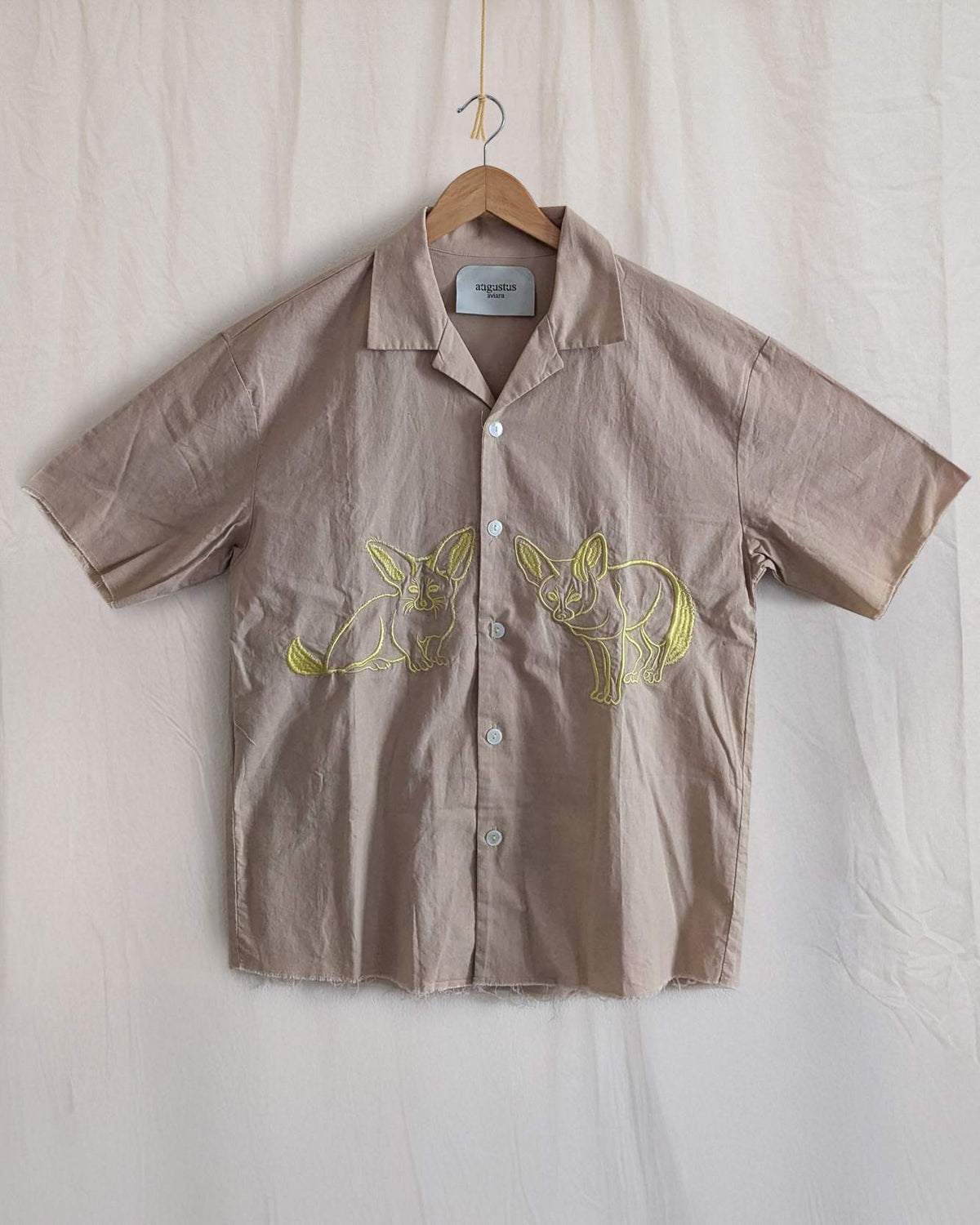 Brown shirt with yellow fox designs on a hanger against a beige background