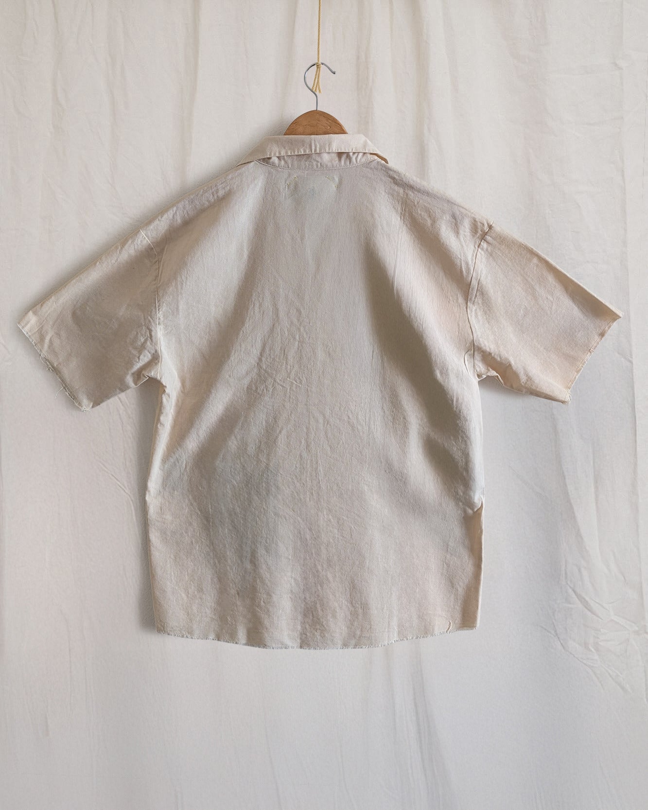 Beige shirt with a label on a hanger against a white background
