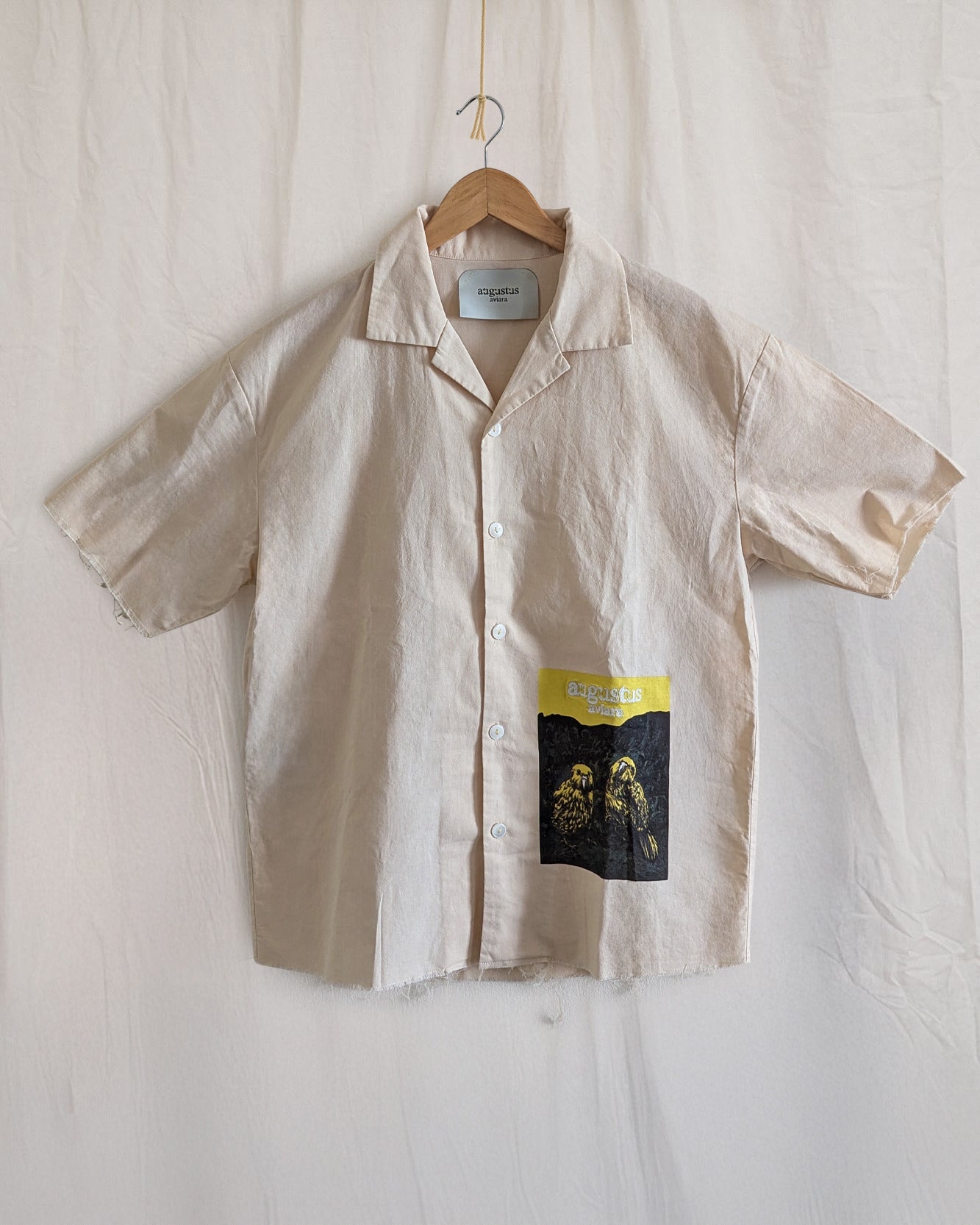 Beige shirt with a label on a hanger against a white background